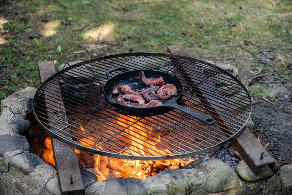 Perfectly grilled octopus tentacles sizzling over a campfire in a cast-iron pan, ideal for outdoor cooking enthusiasts.